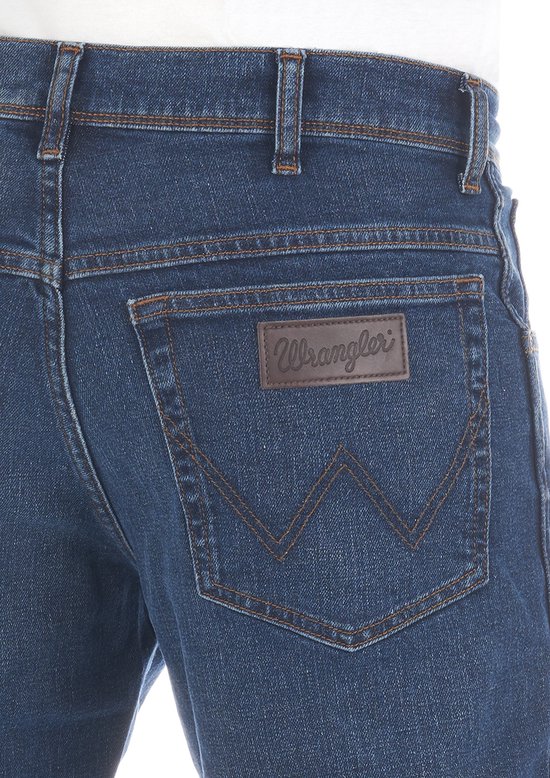 Achterkant van een blauwe jeans met bruin Wrangler logo op een leren patch en koperkleurige stiksels.