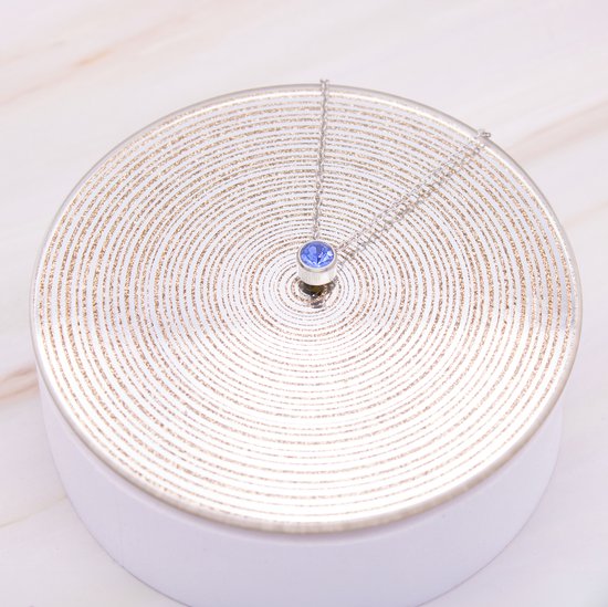 Collier argenté avec pendentif en zircone bleue sur plateau.