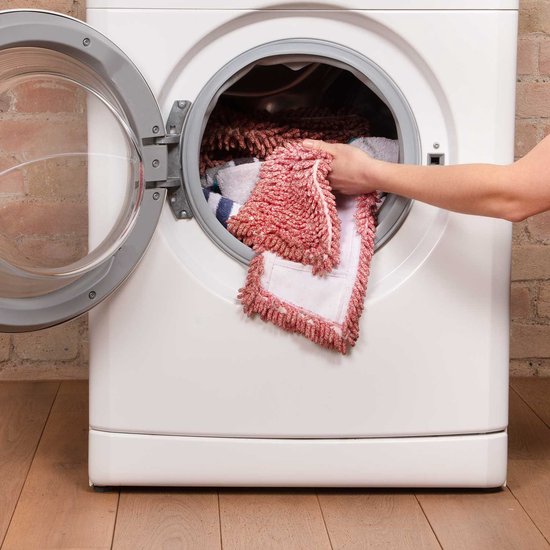 Main plaçant une serpillière en microfibre rouge et blanche dans une machine à laver ouverte.