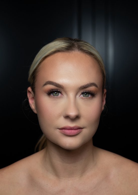 Model met blond haar, groene ogen, en subtiele make-up, lachend naar de camera.