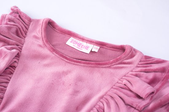 Nekdetail van een roze fluwelen jurk met ruches en label 'Someone'.