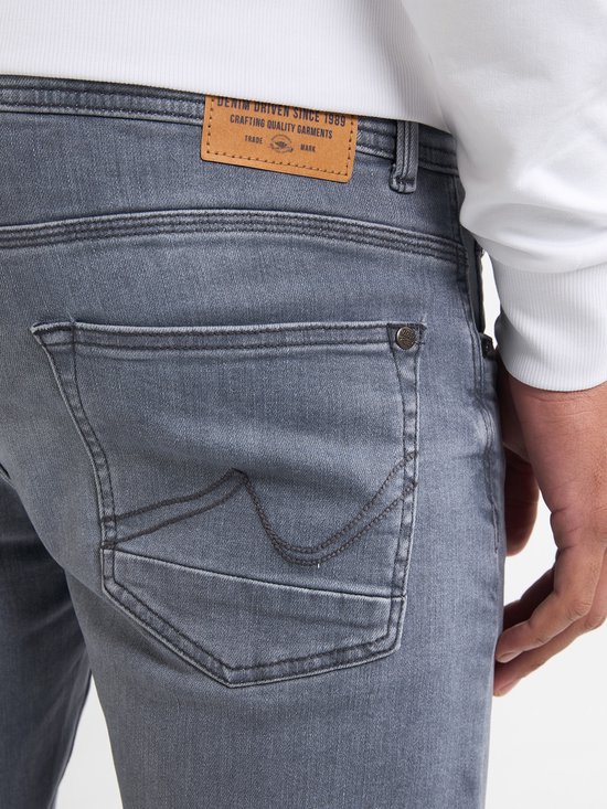 Detail van de achterzak van een grijze jeans met een bruin leren label 'DENIM DRIVEN SINCE 1989 CRAFTING QUALITY GARMENTS'.