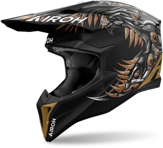 Casque de cross Airoh noir avec un design cyborg/dragon en bronze, gris et blanc. Le casque a une visière et des aérations.