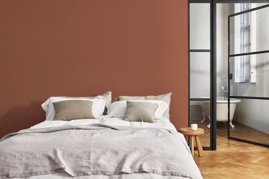 Slaapkamer met terracotta muur, tweepersoonsbed en een glazen deur naar een badkamer.