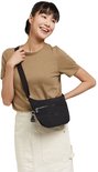 Vrouw draagt zwarte Kipling schoudertas, model Arto S, met zilverkleurige ritsen en Kipling aapje als hanger. Ze draagt een bruin T-shirt en een crème rok.