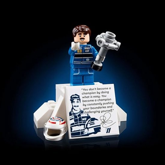 Nigel Mansell Lego minifiguur met helm en trofee, staand op een witte basis.