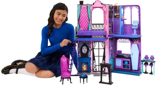 Meisje zit bij een paars en roze poppenhuis met meubels en accessoires.