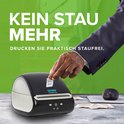 Een hand met een sushikostuum die een etiket uit een zwarte en witte DYMO LabelWriter 5XL labelprinter haalt. Tekst: KEIN STAU MEHR. DRUCKEN SIE PRAKTISCH STAUFREI.