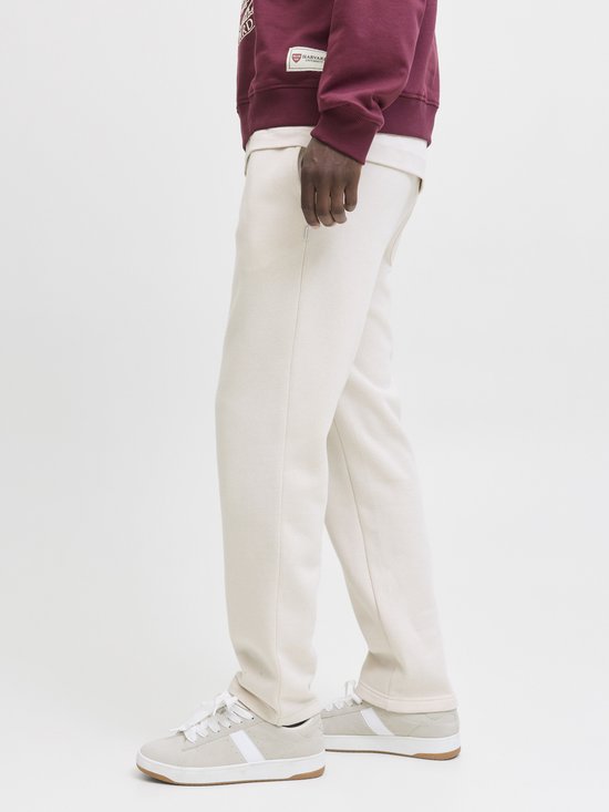 Man met crème joggingbroek en witte sneakers met strepen, zij-aanzicht.