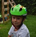 Lichtgroene kinderfietshelm met dinosaurusprint, grote blauwe ogen en scherpe tanden. Een jongen draagt de helm.
