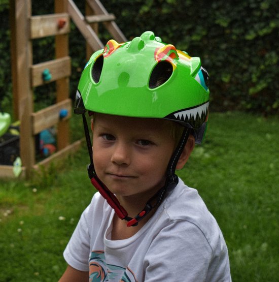 Lichtgroene kinderfietshelm met dinosaurusprint, grote blauwe ogen en scherpe tanden. Een jongen draagt de helm.