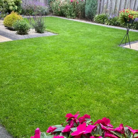 Een strak gemaaid, groen gazon met bloeiende roze bloemen op de voorgrond en diverse planten en bloemen op de achtergrond.