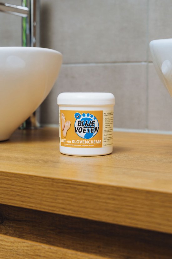 Potje Blije Voeten eelt- en klovencrème op een houten plank in een badkamer, naast een wasbak.