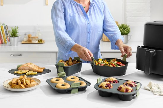 Vrouw in keuken met diverse bakvormen, waaronder een donkergrijze muffinvorm met 4 bessenmuffins.