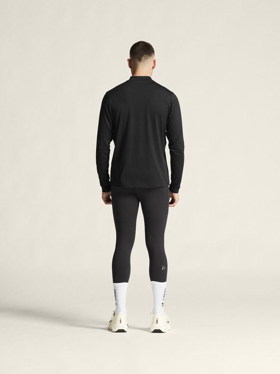 Man van achteren gezien in een zwarte longsleeve en zwarte sportlegging. Draagt witte sokken en sneakers.