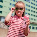 Une fille avec des lunettes de soleil en forme de cœur et la langue tirée, tient une bouteille Kambukka rose avec un imprimé de chiens.