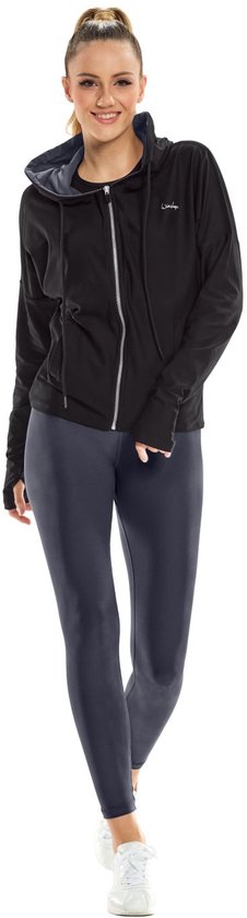 Model in zwart vest met capuchon, wit sporttopje en donkergrijs legging.