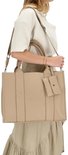 Vrouw met beige handtas met 'CHARM LONDON' logo, draagt deze crossbody met schouderband.