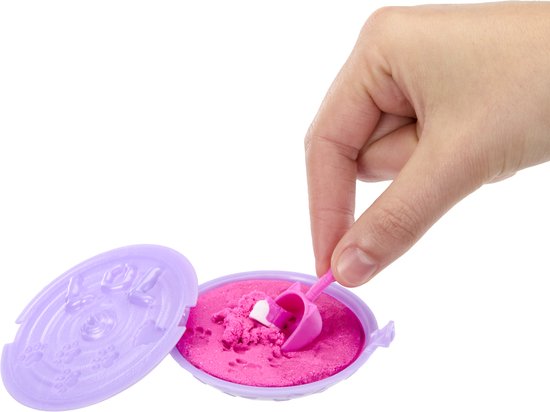 Hand gebruikt roze schepje om roze kinetisch zand te scheppen uit een paars bakje met L.O.L. logo.