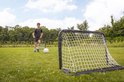 Jongen traint met voetbal en twee voetbaldoelen op grasveld
