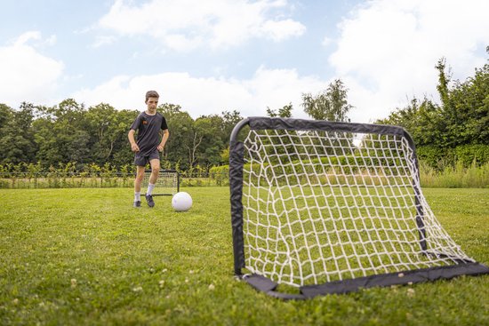 Jongen traint met voetbal en twee voetbaldoelen op grasveld