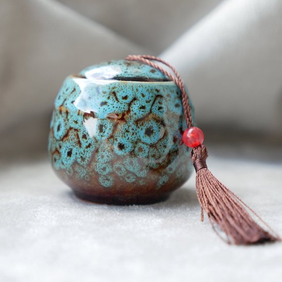 Turquoise mini-urn met een glanzende, gespikkelde afwerking, bruine kwast en rode kraal.