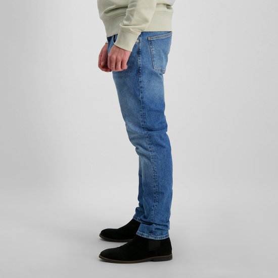 Jean bleu délavé clair, porté par un mannequin avec des baskets blanches et des chaussures noires.