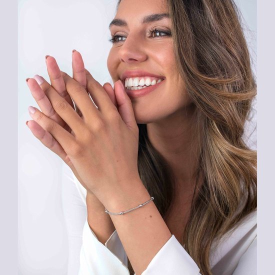 Zilverkleurige armband met dunne ketting en subtiele bolletjes, gedragen door een lachende vrouw.