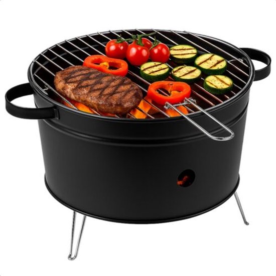 Barbecue rond noir avec steak, légumes grillés et tomates au-dessus de braises chaudes.