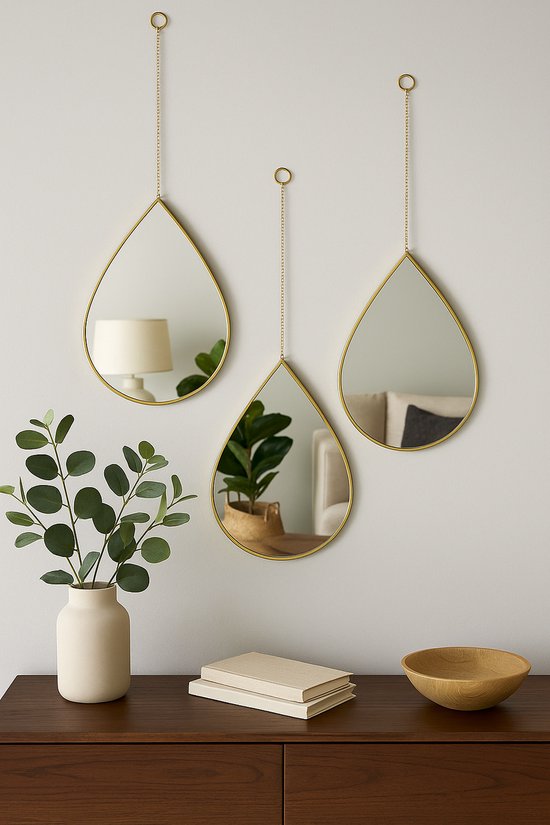 Drie druppelvormige spiegels met gouden frame hangend aan een muur met een vaas en plant.