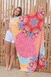 Vrouw met witte top en korte broek staat voor een houten hek en houdt een groot strandlaken met mandala print vast.