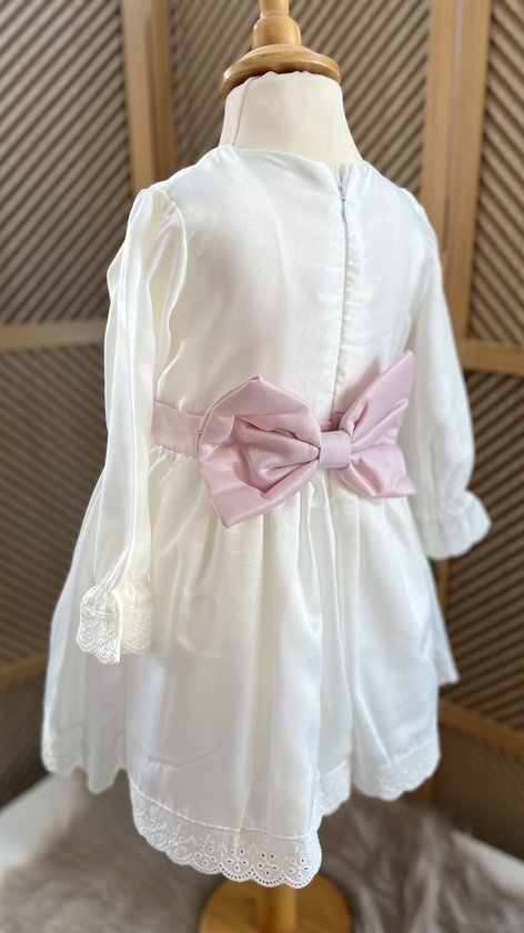Witte jurk met roze strik op de rug, lange mouwen met kanten manchetten.