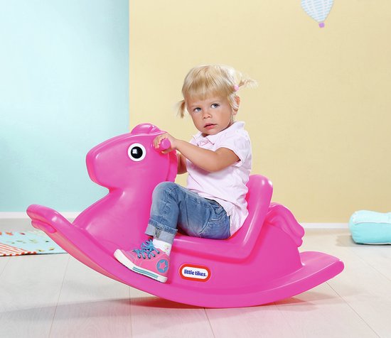 Een jong meisje met blonde staartjes, in een roze shirt en spijkerbroek, op een roze Little Tikes hobbelpaard.