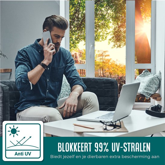 Man met telefoon in blauw overhemd, laptop en bril, kijkt naar buiten. Blokkeert 99% UV-stralen.