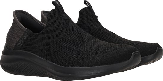 Close-up van twee zwarte Skechers slip-on sneakers met gebreid bovenwerk en grijze hiel.
