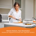 Une femme coupe un oignon dans une cuisine, avec un couvercle de micro-ondes gris pliable contenant de la nourriture posé sur le comptoir.