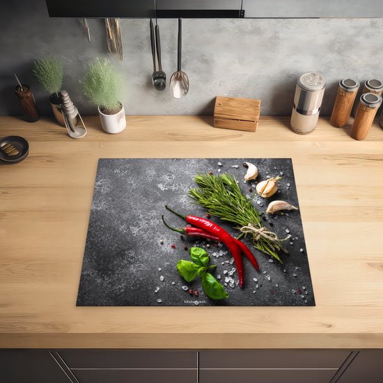 Inductiebeschermer met betonprint, met rode pepers, knoflook en kruiden, op een houten aanrecht.