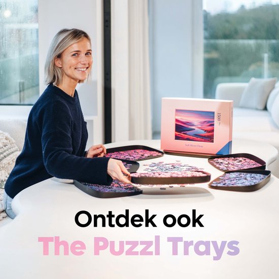 Een glimlachende vrouw zit aan tafel met puzzelbakjes en de Puzzl Trays verpakking, met de tekst 'Ontdek ook The Puzzl Trays'.