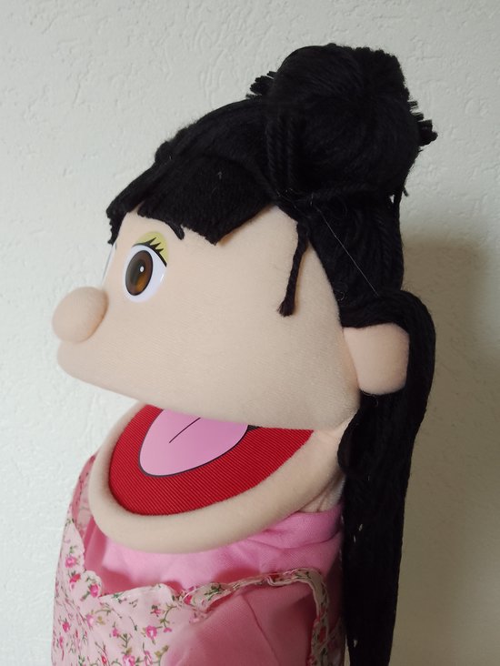 Profiel van een handpop met zwart haar in knotjes, bruine ogen en roze jurkje.