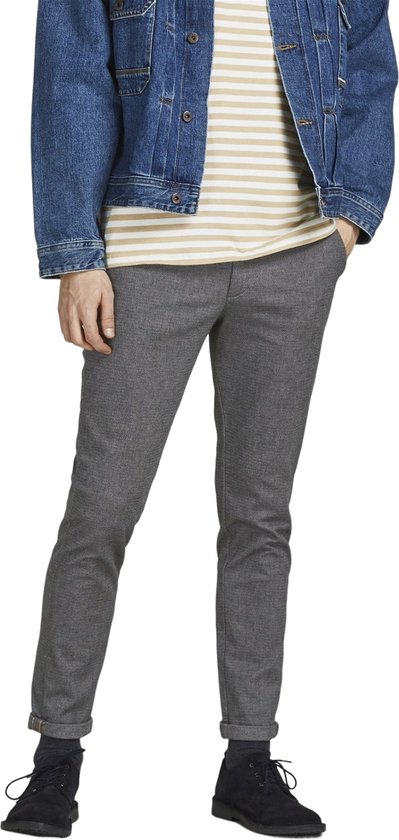 Model in grijze broek met visgraatpatroon, gestreepte top en spijkerjack.
