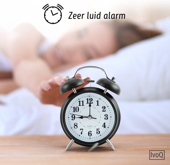 Zwarte wekker op een houten tafel, met een slapend kind op de achtergrond. Tekst: 'Zeer luid alarm'.