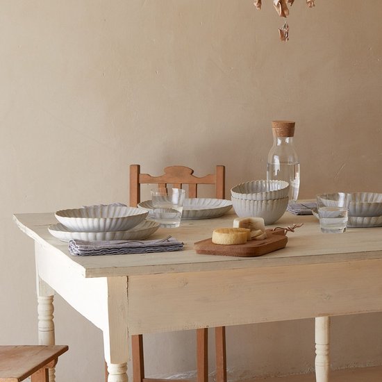 Gedekte tafel met crème keramische borden, kommen, glazen en waterfles.