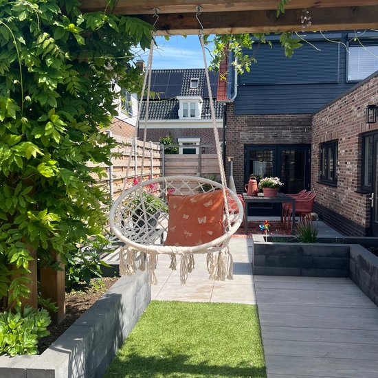 Gebroken wit macramé hangstoel met franjes en een oranje kussen met vlinders.