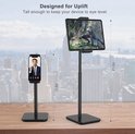 Zwarte, in hoogte verstelbare tablet- en telefoonstandaard op een bureau. Tablet: 53,6 cm hoog, telefoon: 34,5 cm hoog.