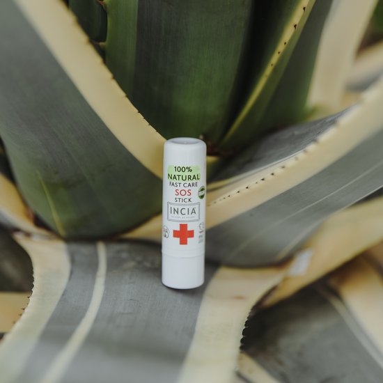 Witte SOS stick van INCIA met rode kruis en groene tekst '100% NATURAL FAST CARE SOS STICK' voor een agavesplant.