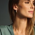 Een vrouw draagt gouden, rechthoekige oorbellen bezet met zirkonen.