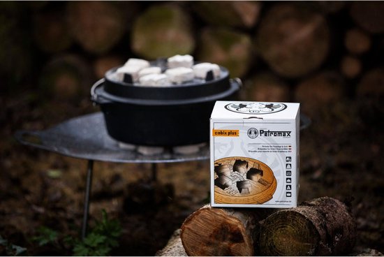 Petromax Dutch oven met witte briketten op deksel, naast een doos Petromax cabix plus briketten. Buiten, met houtblokken.