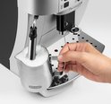 Hand houdt RVS kannetje met melkschuim vast bij de zilverkleurige volautomaat.