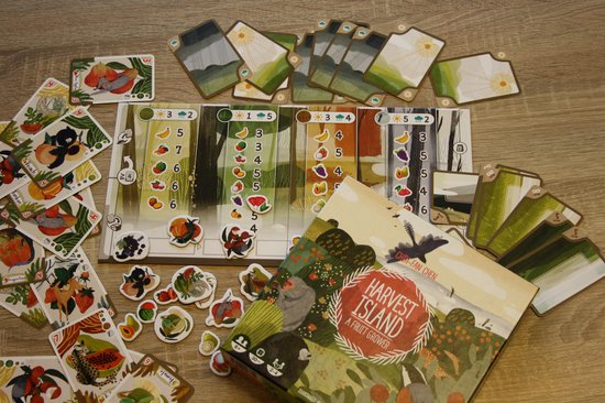 Het spel Harvest Island met doos, kaarten en speelbord, verspreid over een houten tafel.