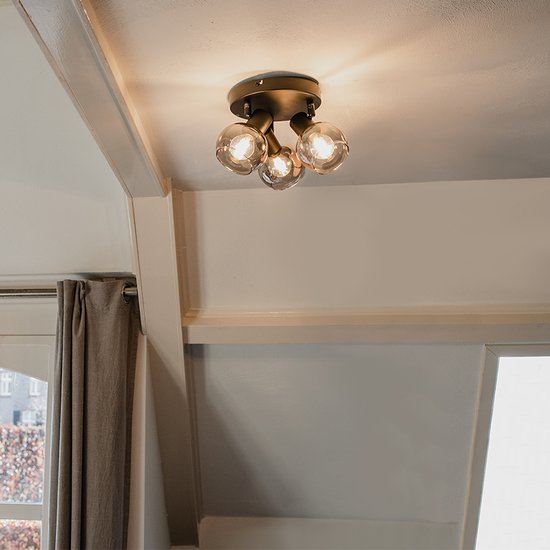 Een plafondlamp met drie glazen bollen, gemonteerd op een zwarte basis in een kamer met een schuin dak.